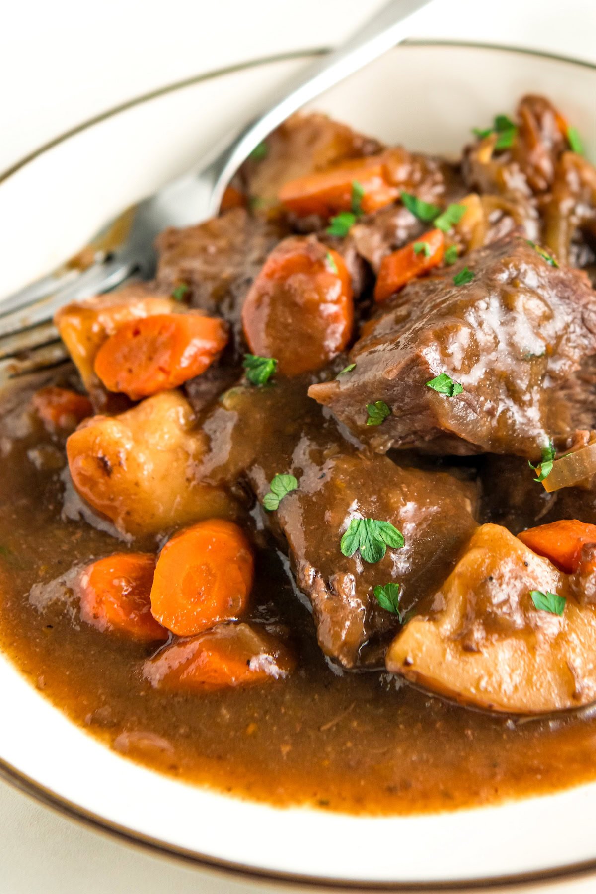 Tender cooked vegetables are plated with slow cooker pot roast and gravy.