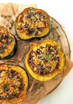 Several servings of sausage stuffed acorn squash on a round serving platter topped with fresh herbs.