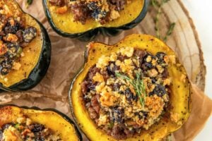 Several servings of sausage stuffed acorn squash on a round serving platter topped with fresh herbs.