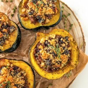 Several servings of sausage stuffed acorn squash on a round serving platter topped with fresh herbs.