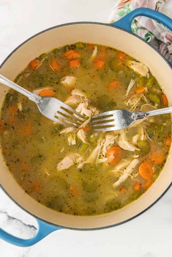 Two forks are shredding cooked chicken in a soup pot.