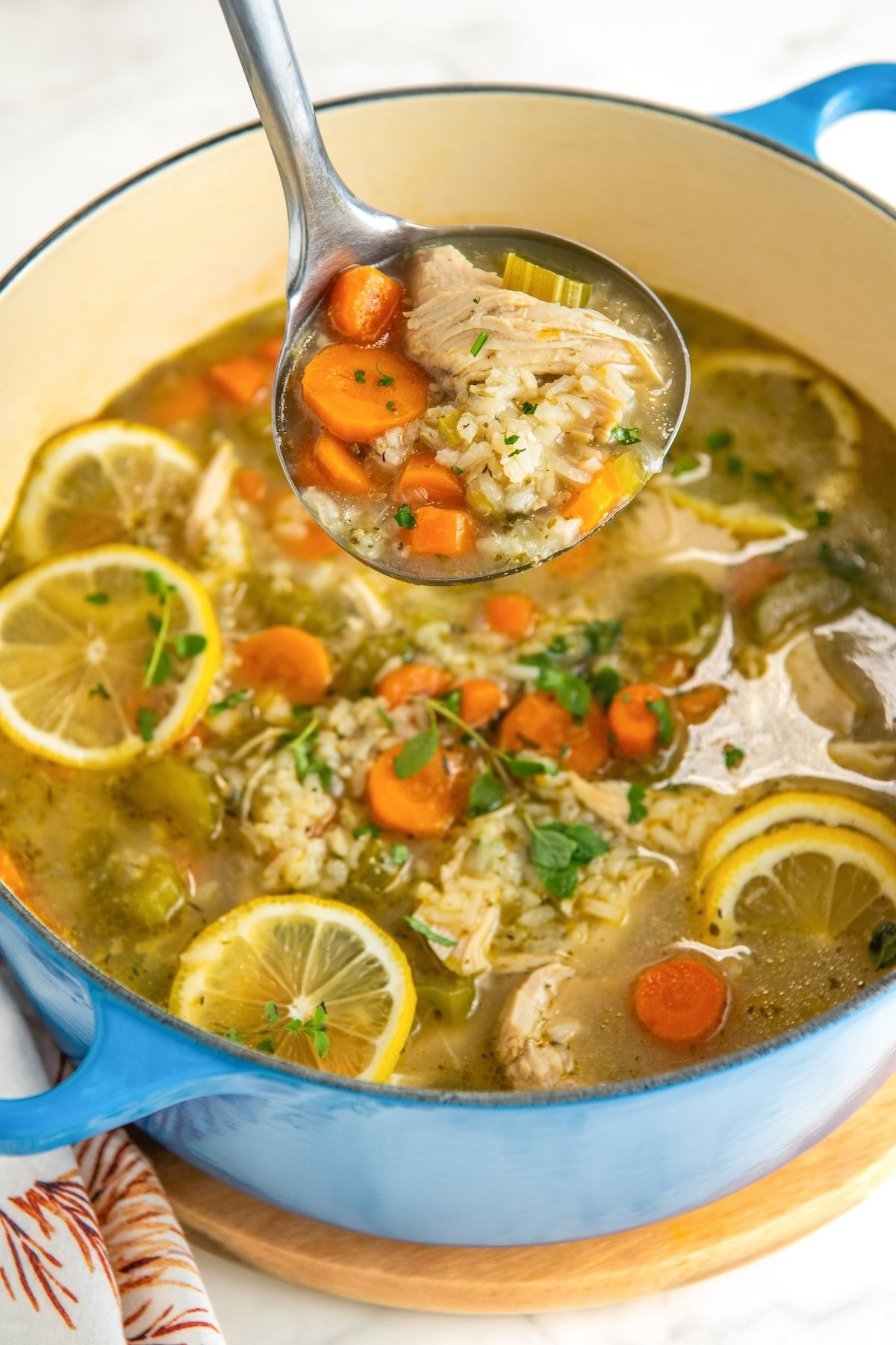 A ladle is lifting a portion of soup from a pot filled with lemon chicken rice soup.