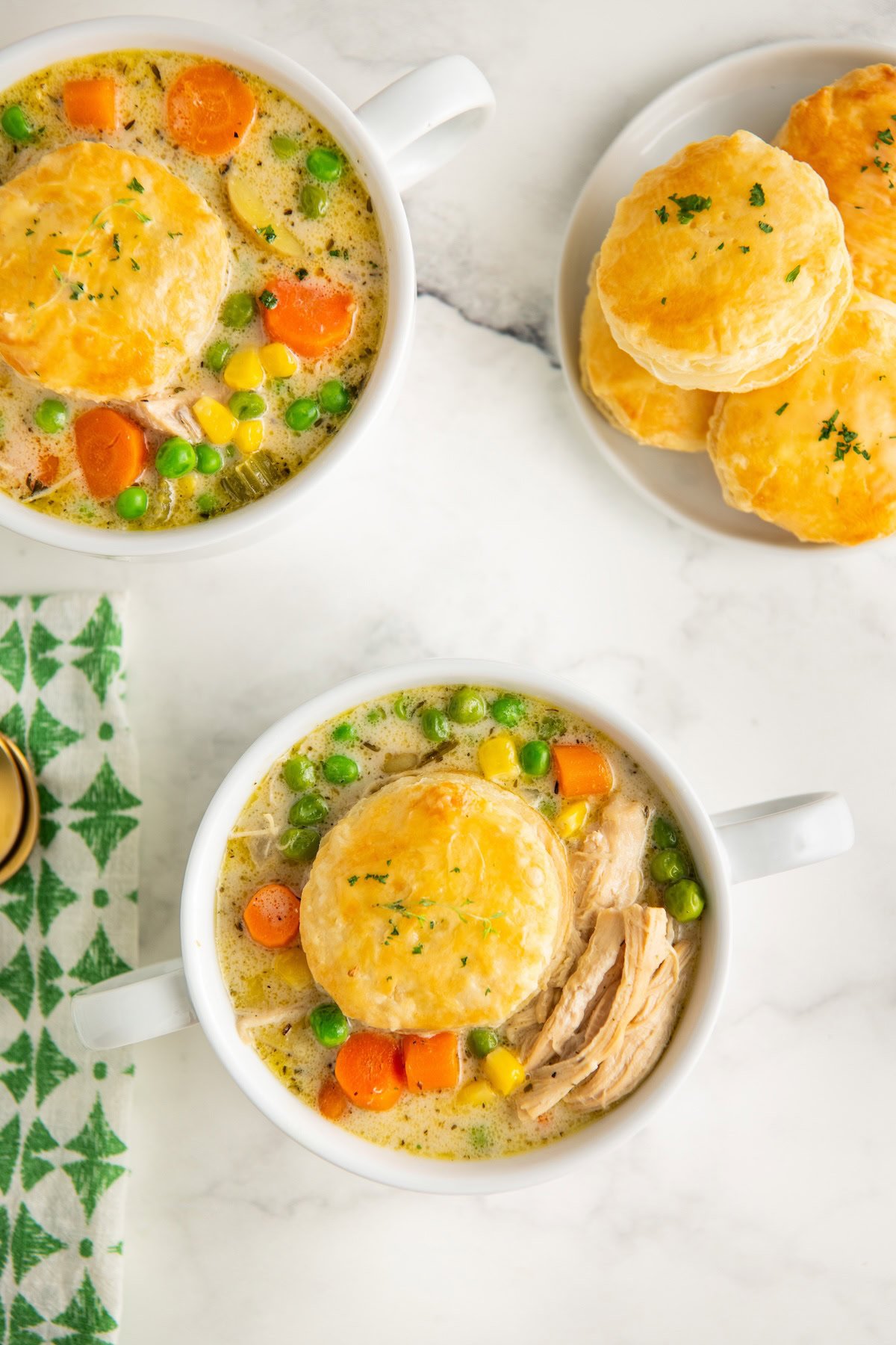 Garnished bowls of creamy chicken pot pie soup on a white surface.