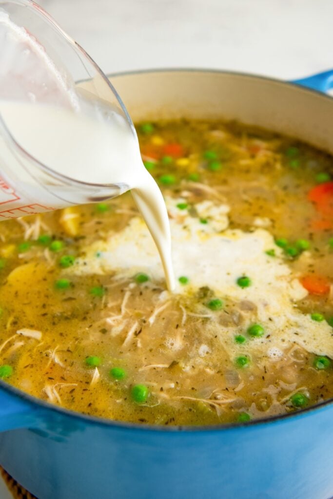 Heavy cream is being poured into the pot filled with soup.