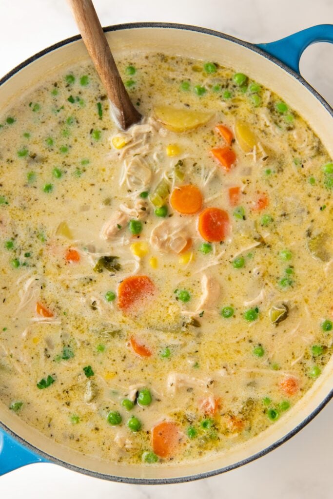 Creamy chicken soup is stirred in a large dutch oven.