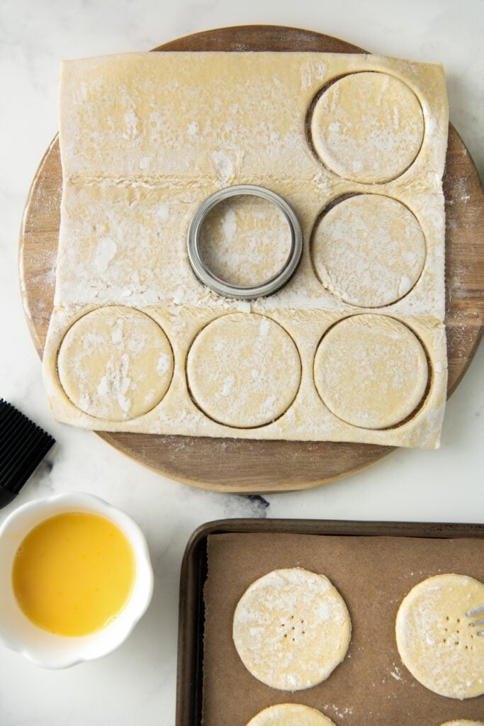 A biscuit cutter is slicing round circles of puff pastry from a sheet.