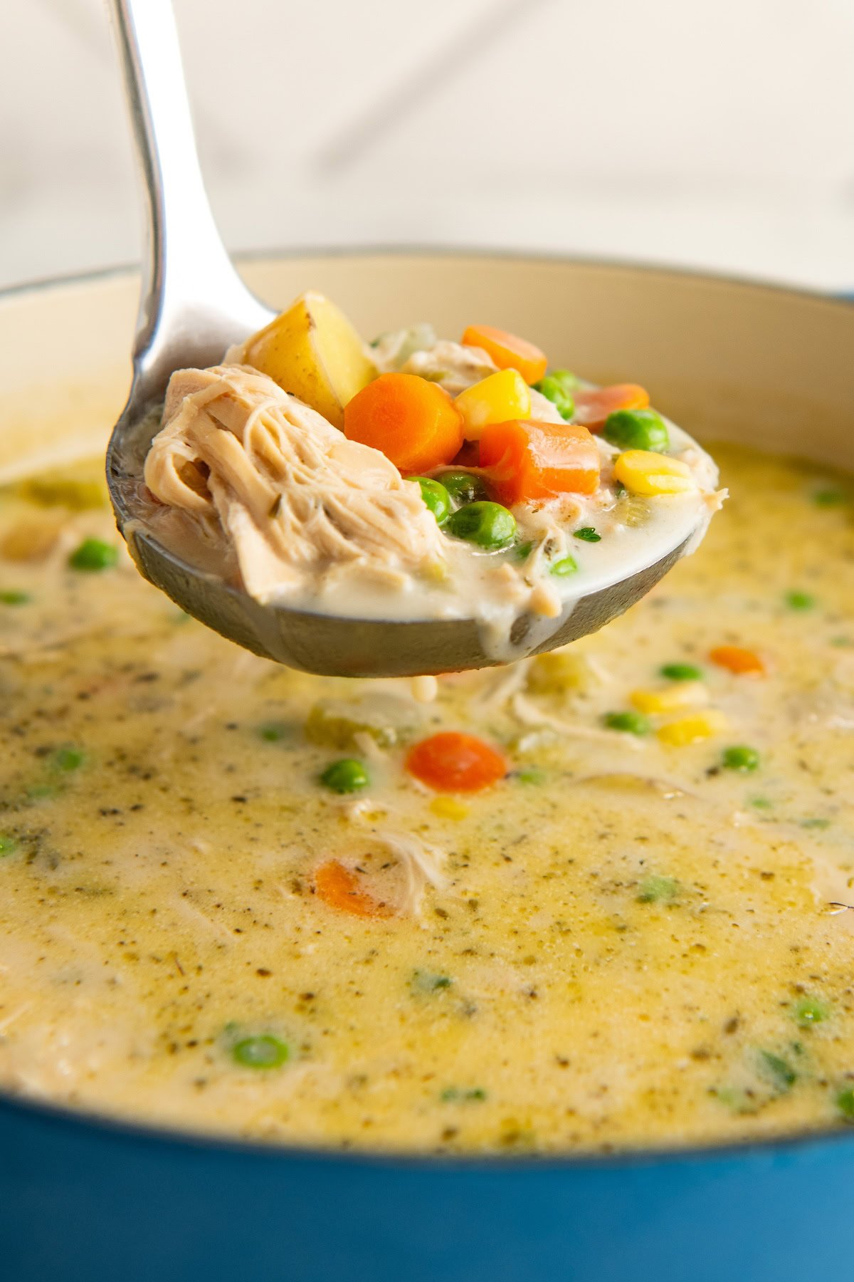 A ladle is scooping a portion of chicken pot pie soup from the dutch oven.