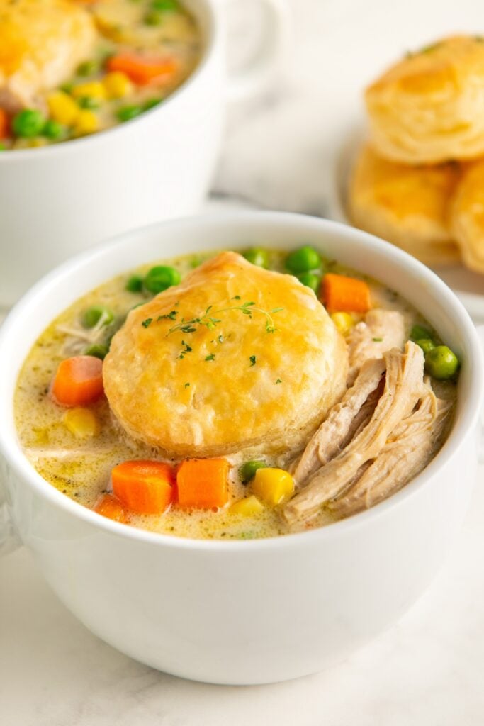 A golden puff pastry biscuit and fresh herbs garnish a bowl of chicken pot pie soup.