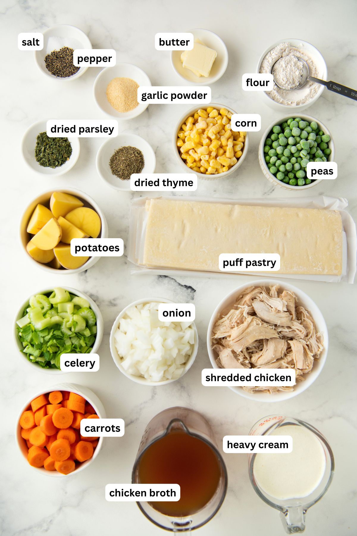 Ingredients for chicken pot pie soup recipe in order from top to bottom: salt, pepper, butter, flour, garlic powder, dried parsley, dried thyme, corn, peas, potatoes, puff pastry, celery, onion, shredded chicken, carrots, chicken broth, heavy cream.