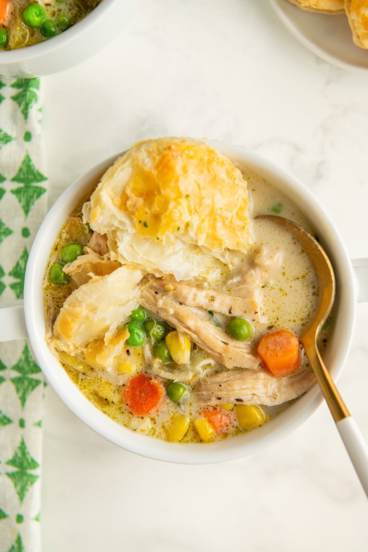 A spoon is placed in a bowl of creamy chicken pot pie soup with puff pastry on top.