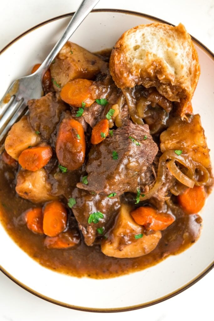 A crusty piece of bread is plated with tender slow cooker pot roast, vegetables, and French onion gravy.