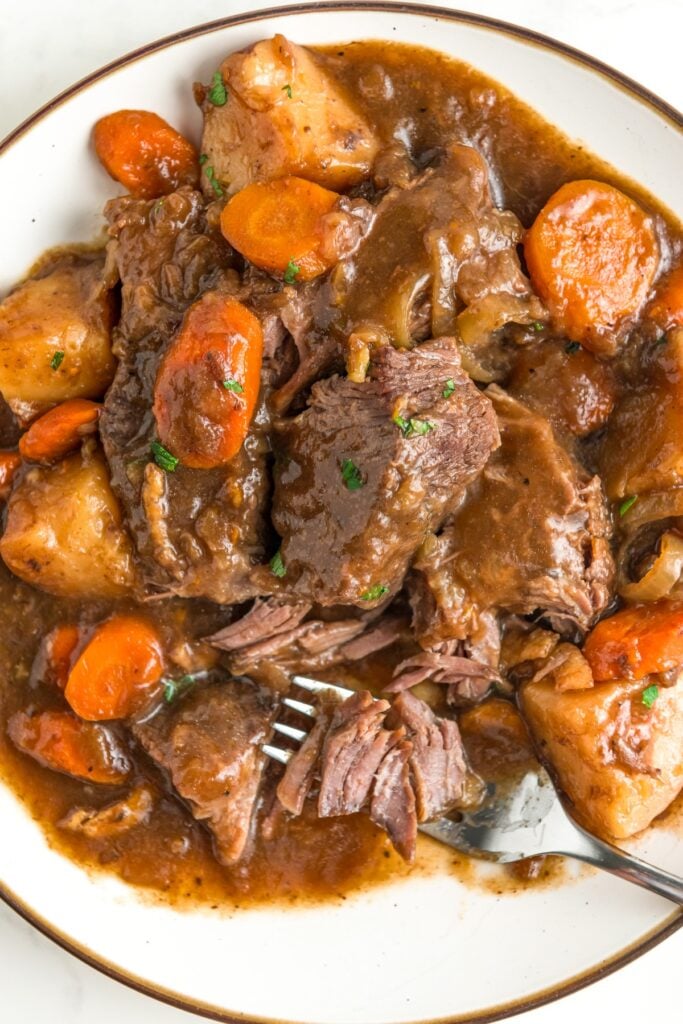 French onion pot roast recipe served with hearty gravy on a plate with a fork cutting a bite.