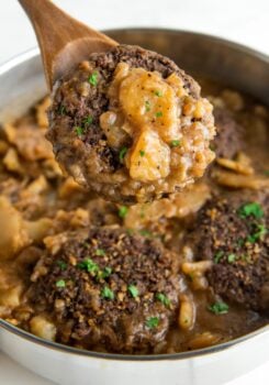 A hamburger steak with thin sliced potatoes and onions are coated in gravy.