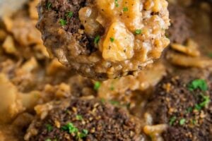 A hamburger steak with thin sliced potatoes and onions are coated in gravy.