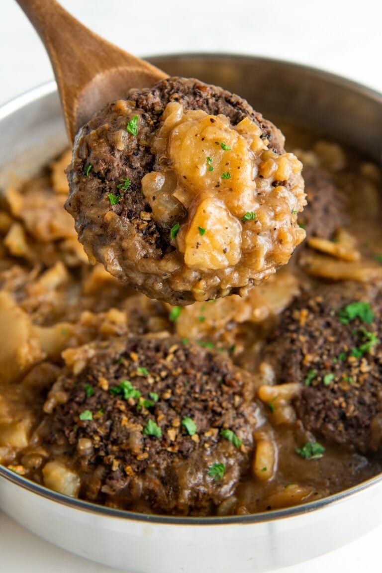 A hamburger steak with thin sliced potatoes and onions are coated in gravy.