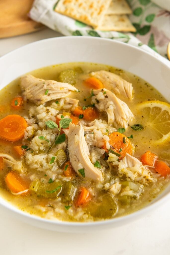 Lemon slices and fresh herbs garnish a bowl filled with lemon chicken rice soup.