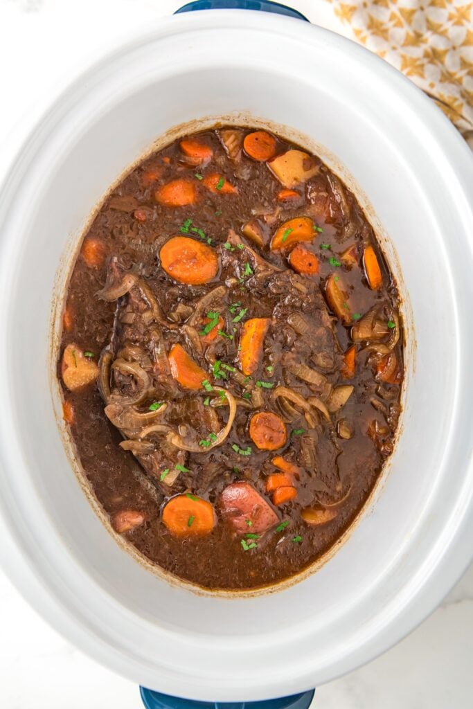 Cooked French onion pot roast presented in a large white slow cooker.