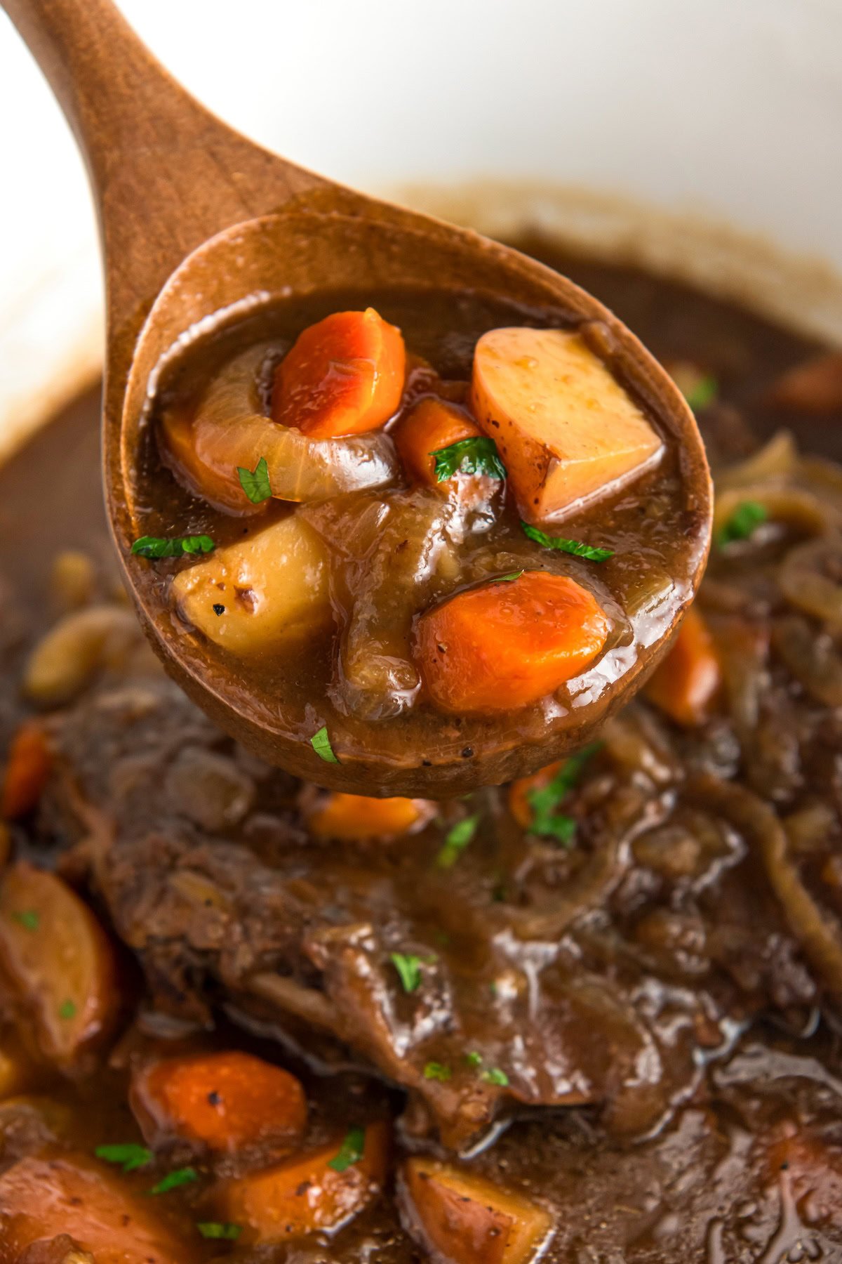 A large spoonful of savory French onion slow cooker pot roast being lifted from a crockpot.