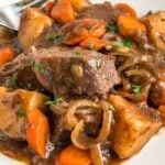 A plate of slow cooker French onion pot roast is garnished with fresh herbs.