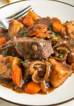 A plate of slow cooker French onion pot roast is garnished with fresh herbs.