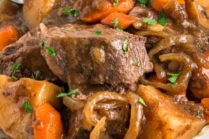 A plate of slow cooker French onion pot roast is garnished with fresh herbs.