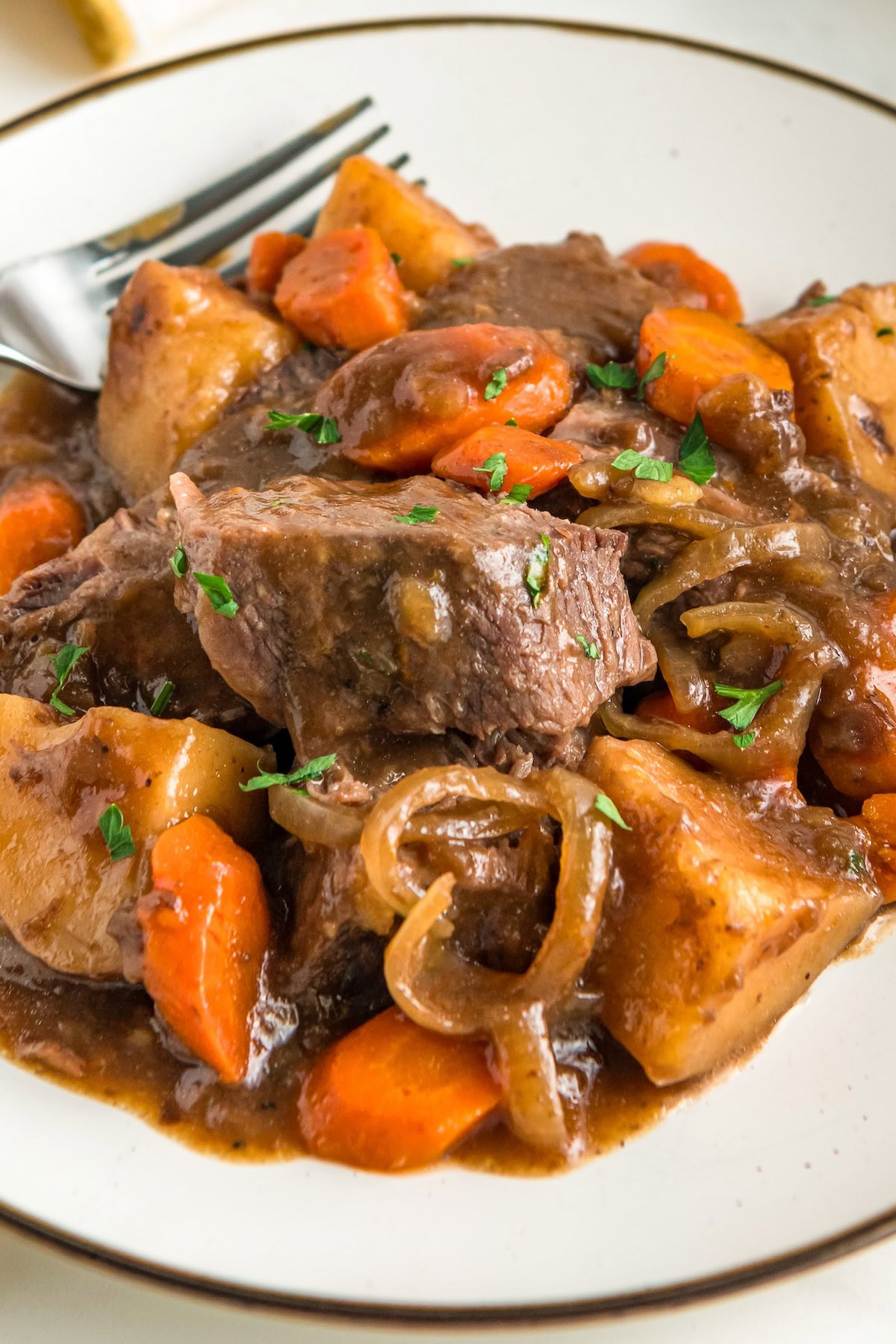 A plate of slow cooker French onion pot roast is garnished with fresh herbs.