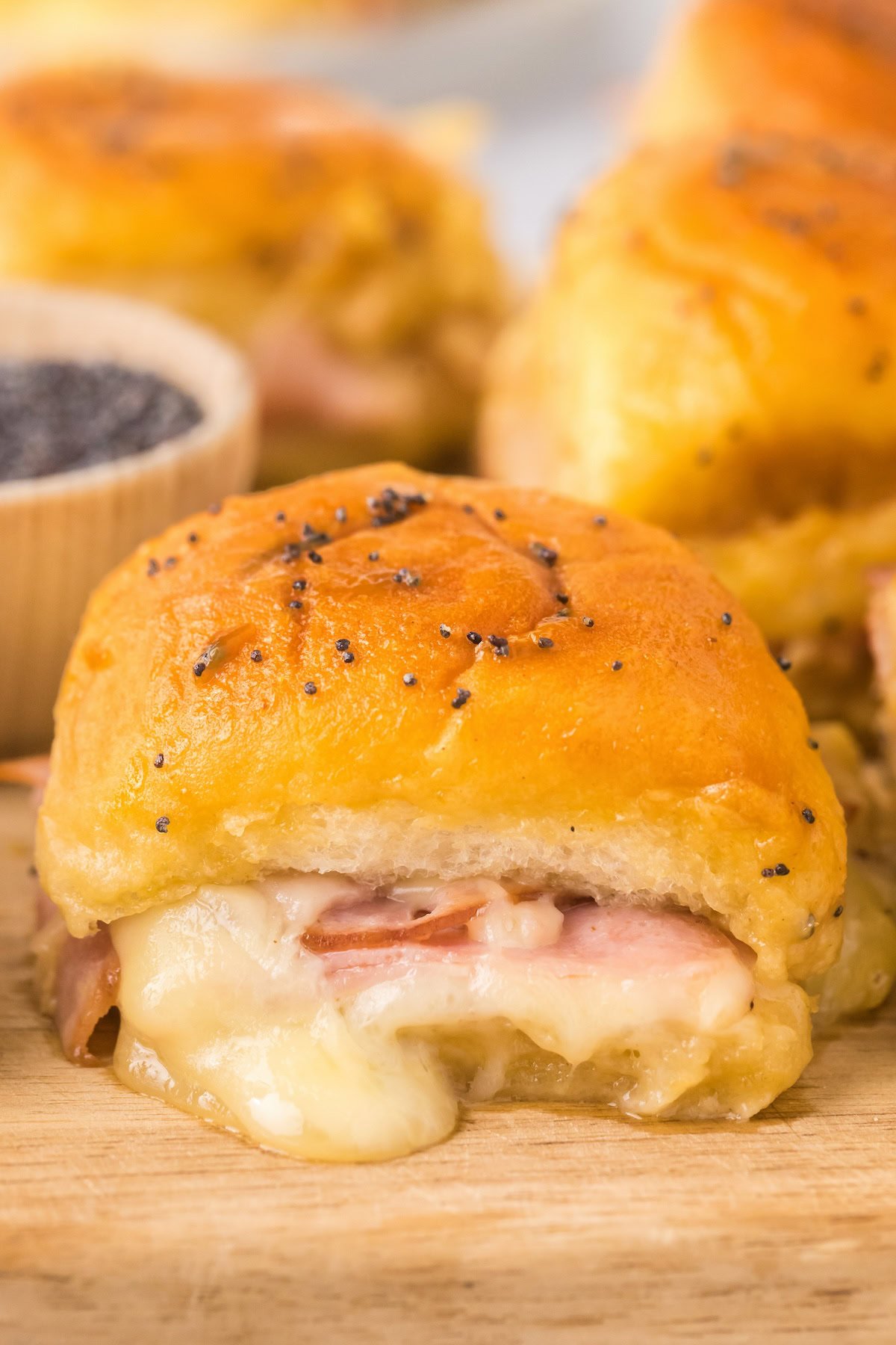 A gooey baked ham and cheese slider is topped with buttery, salty poppy seeds.