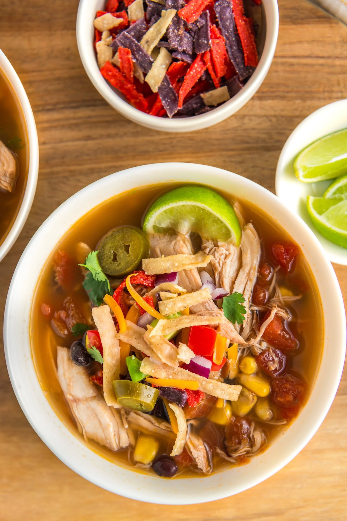 A bowl of garnished slow cooker chicken tortilla soup is presented next to additional toppings.