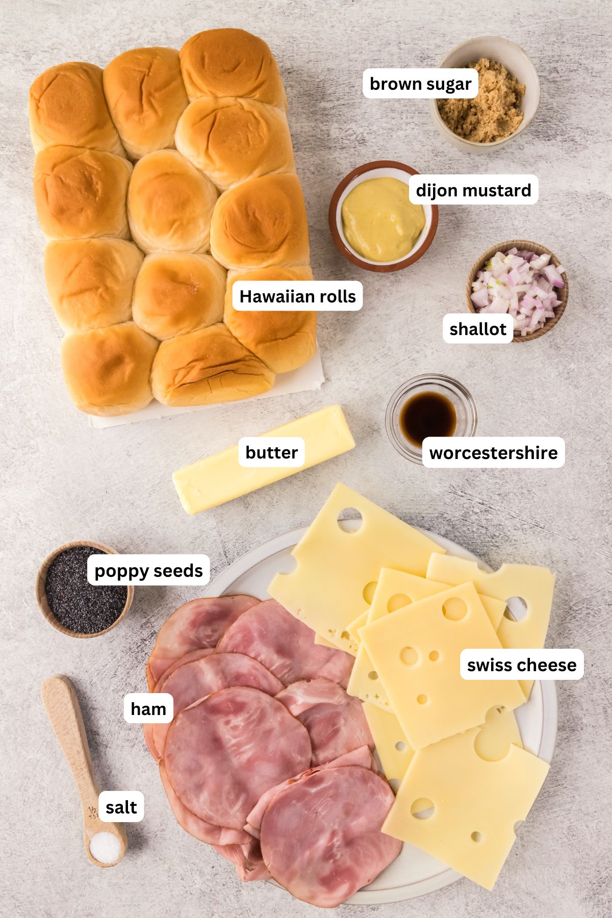 The ingredients for ham and cheese sliders recipe in order from top to bottom: Hawaiian rolls, brown sugar, dijon mustard, shallot, Worcestershire, butter, poppy seeds, ham, Swiss cheese, salt.