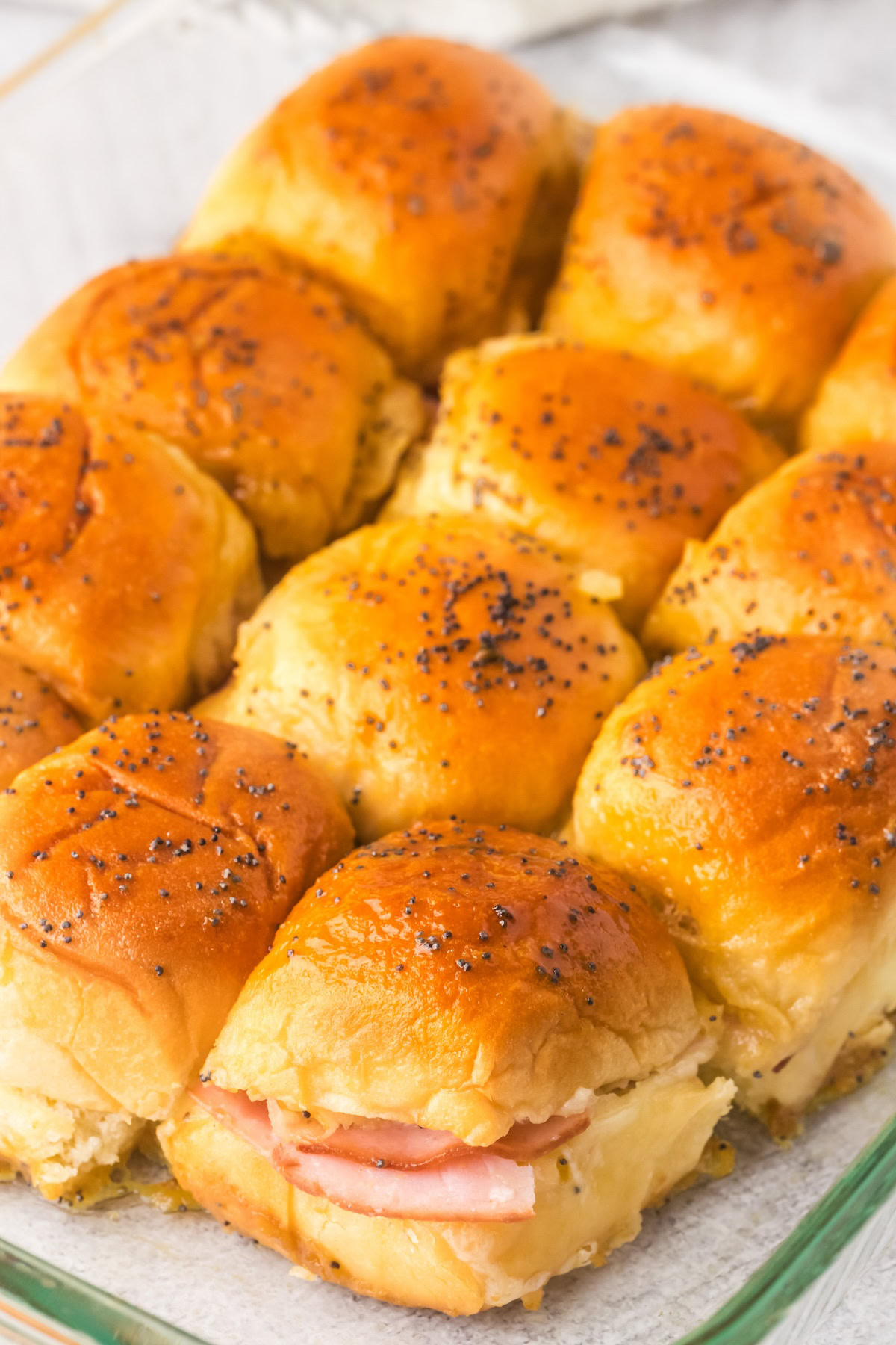 Ham sliders with Swiss cheese are topped with buttery mustard sauce and poppy seeds.