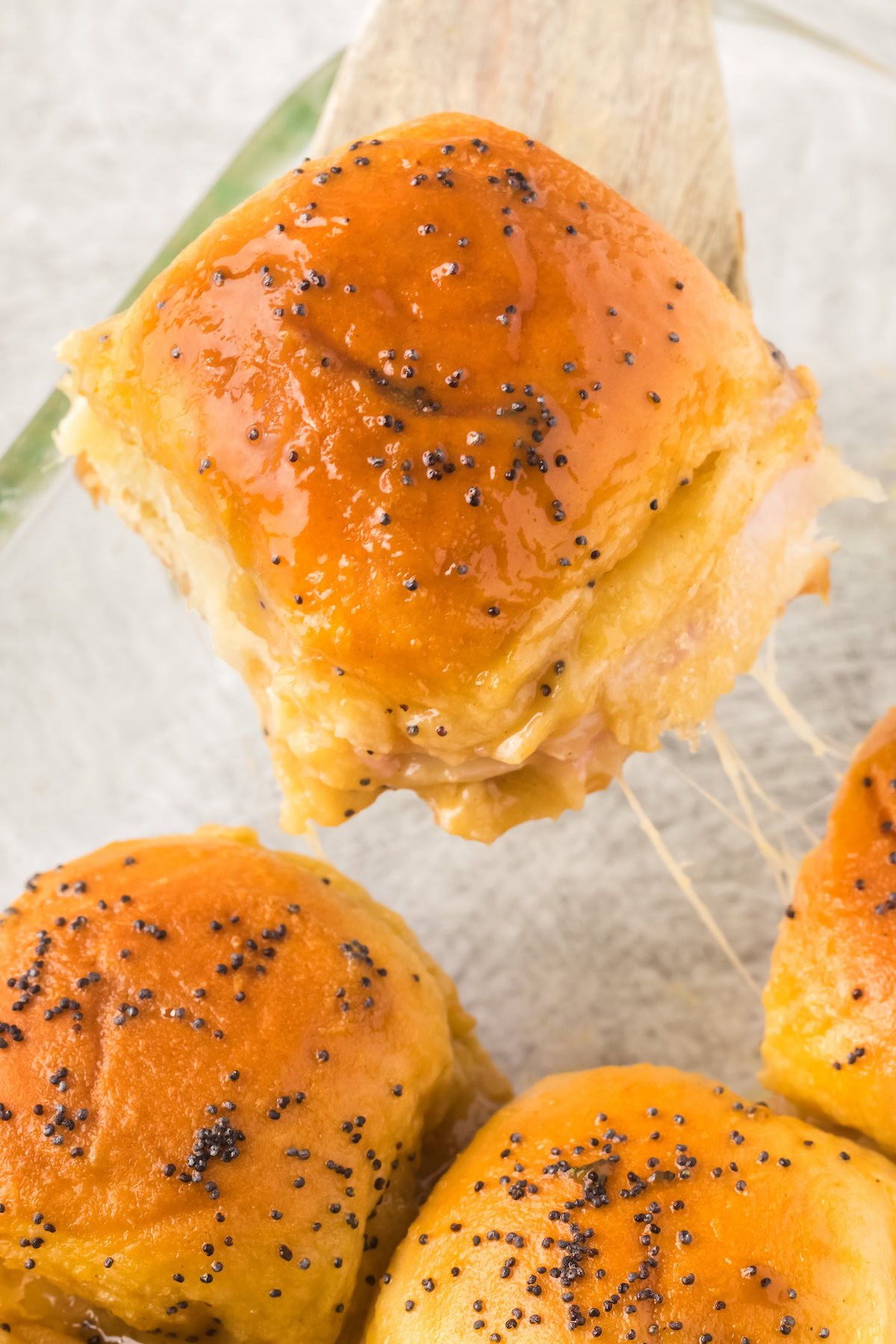 A gooey, cheesy slider is lifted from the baking dish.