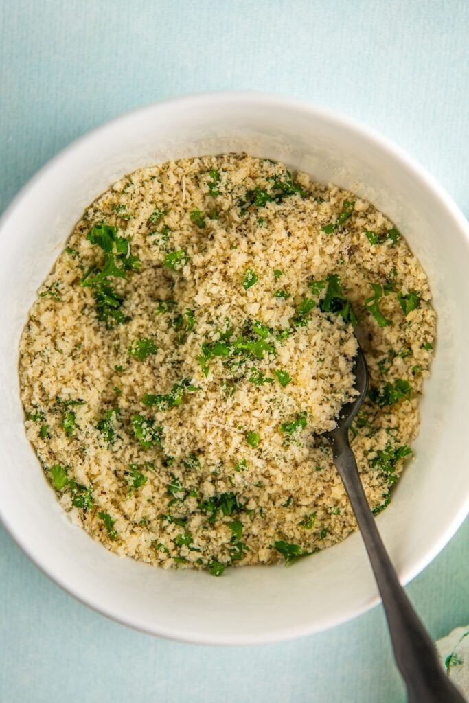 Seasoned breadcrumbs are mixed in a small white bowl.