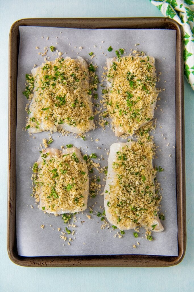 Breadcrumb coated fish filets placed on a parchment paper covered baking sheet.