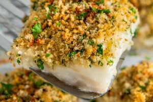 A serving of parmesan crusted cod is being lifted from a sheet pan.