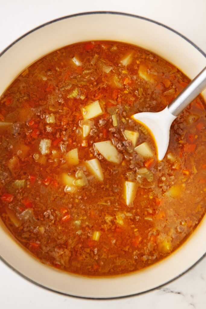 Soup ingredients are being stirred in a large pot.