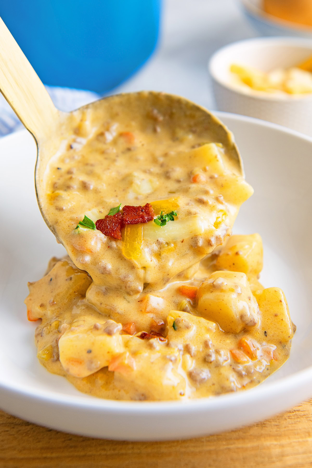 Bacon cheeseburger soup is being ladled into a white bowl.