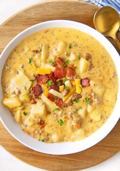 A bowl full of cheeseburger soup is topped with bacon, cheese, and chives.