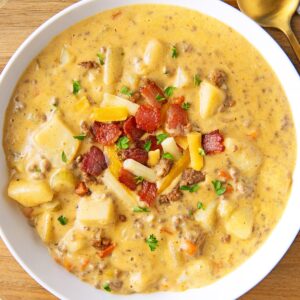 A bowl full of cheeseburger soup is topped with bacon, cheese, and chives.