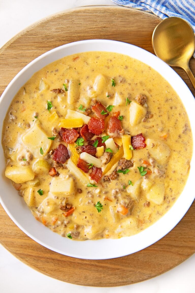 A bowl full of cheeseburger soup is topped with bacon, cheese, and chives.