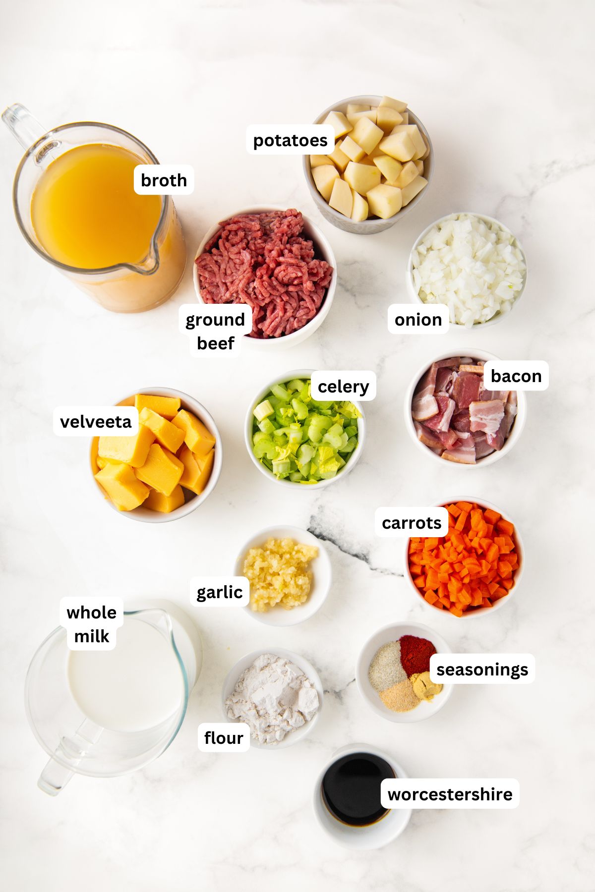 The ingredients for bacon cheeseburger soup recipe in order from top to bottom: broth, potatoes, ground beef, onion, velveeta, celery, bacon, whole milk, garlic, carrots, flour, seasonings, Worcestershire sauce.