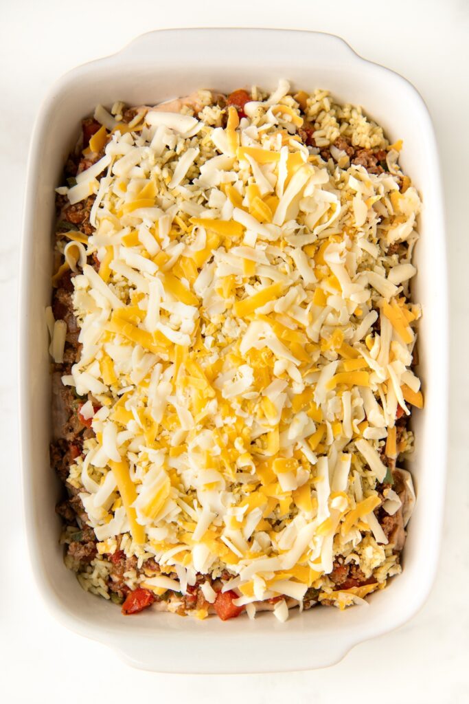 Shredded cheese spread on top of a layered burrito casserole.