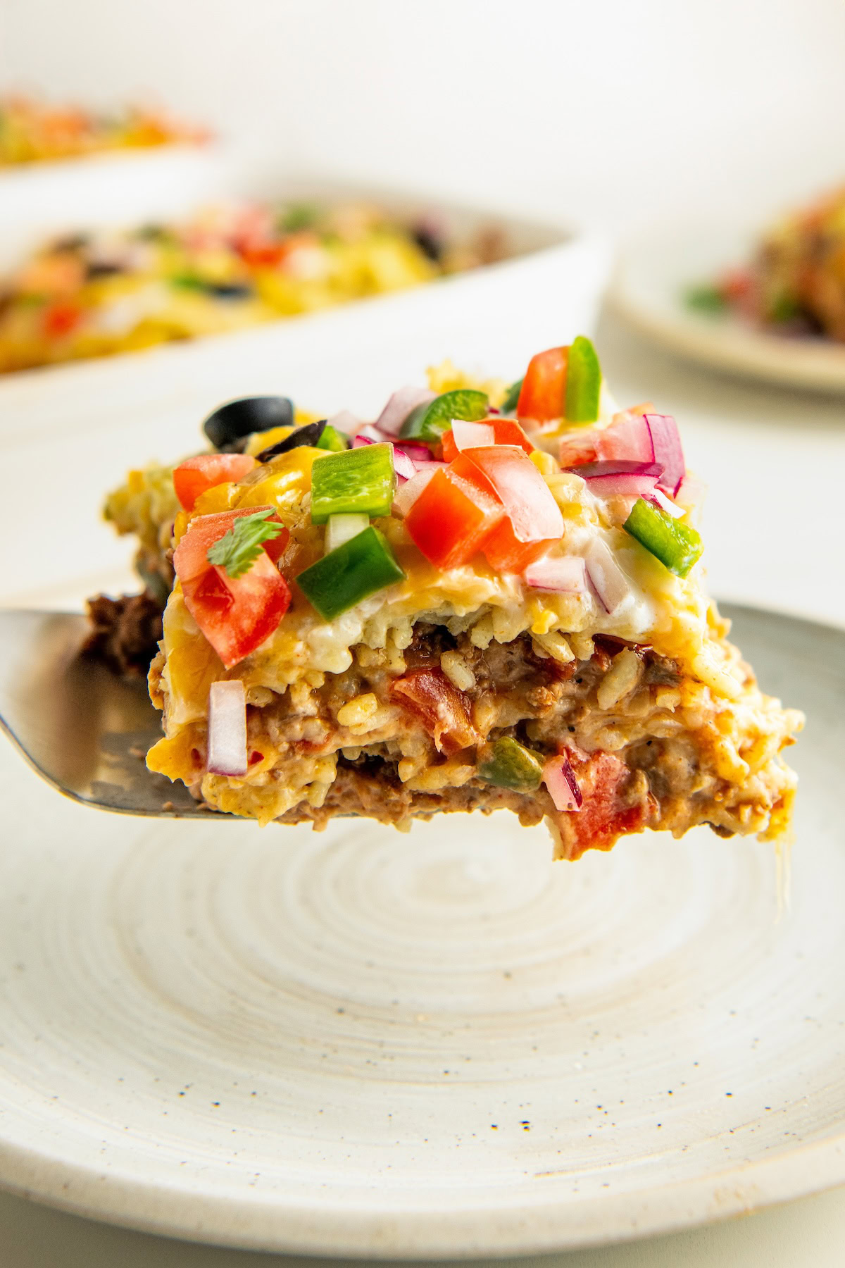 Hearty slice of Tex-Mex casserole lowered onto a plate.