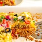 A sliced serving of burrito casserole in a large white baking dish.