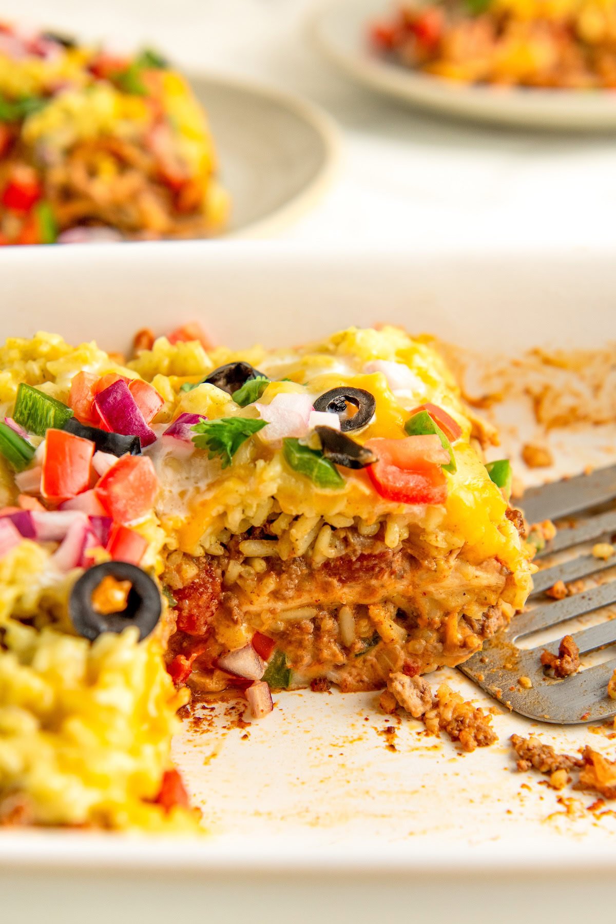 This easy Burrito Casserole recipe combines everything you love about a cheesy, beefy burrito and serves it up in casserole form. A sliced serving of burrito casserole in a large white baking dish.
