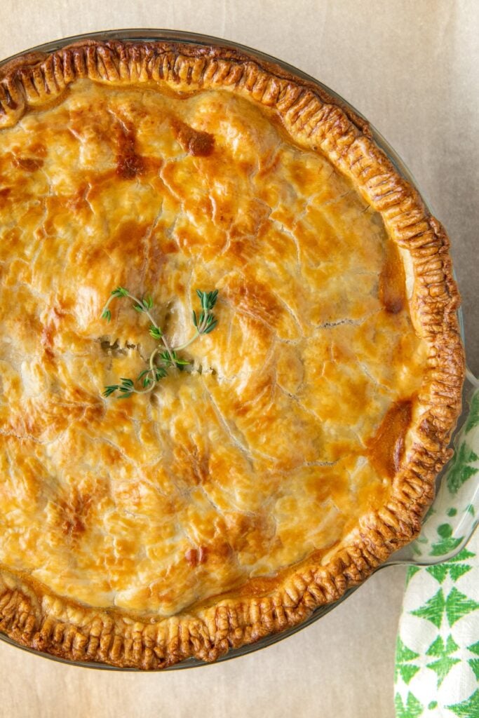 A golden brown chicken pot pie is topped with fresh herbs.