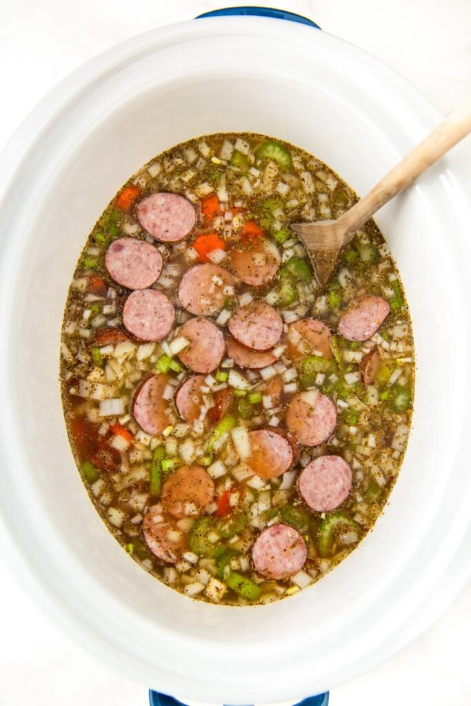 Sausage and bean soup is being stirred in a crockpot.