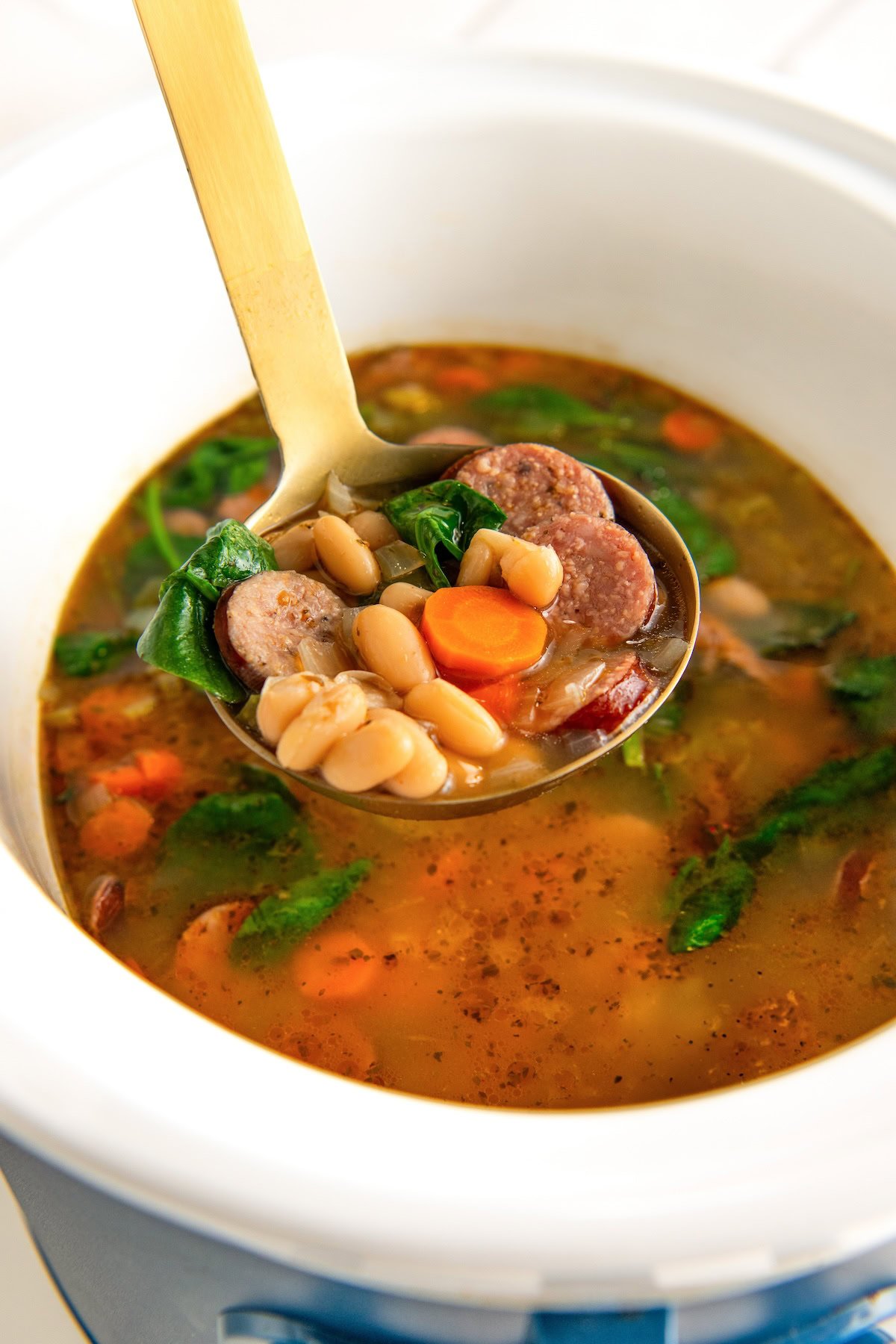 A ladle full of soup is being lifted from the crockpot.