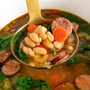 White bean and sausage soup being scooped out of a large slow cooker.