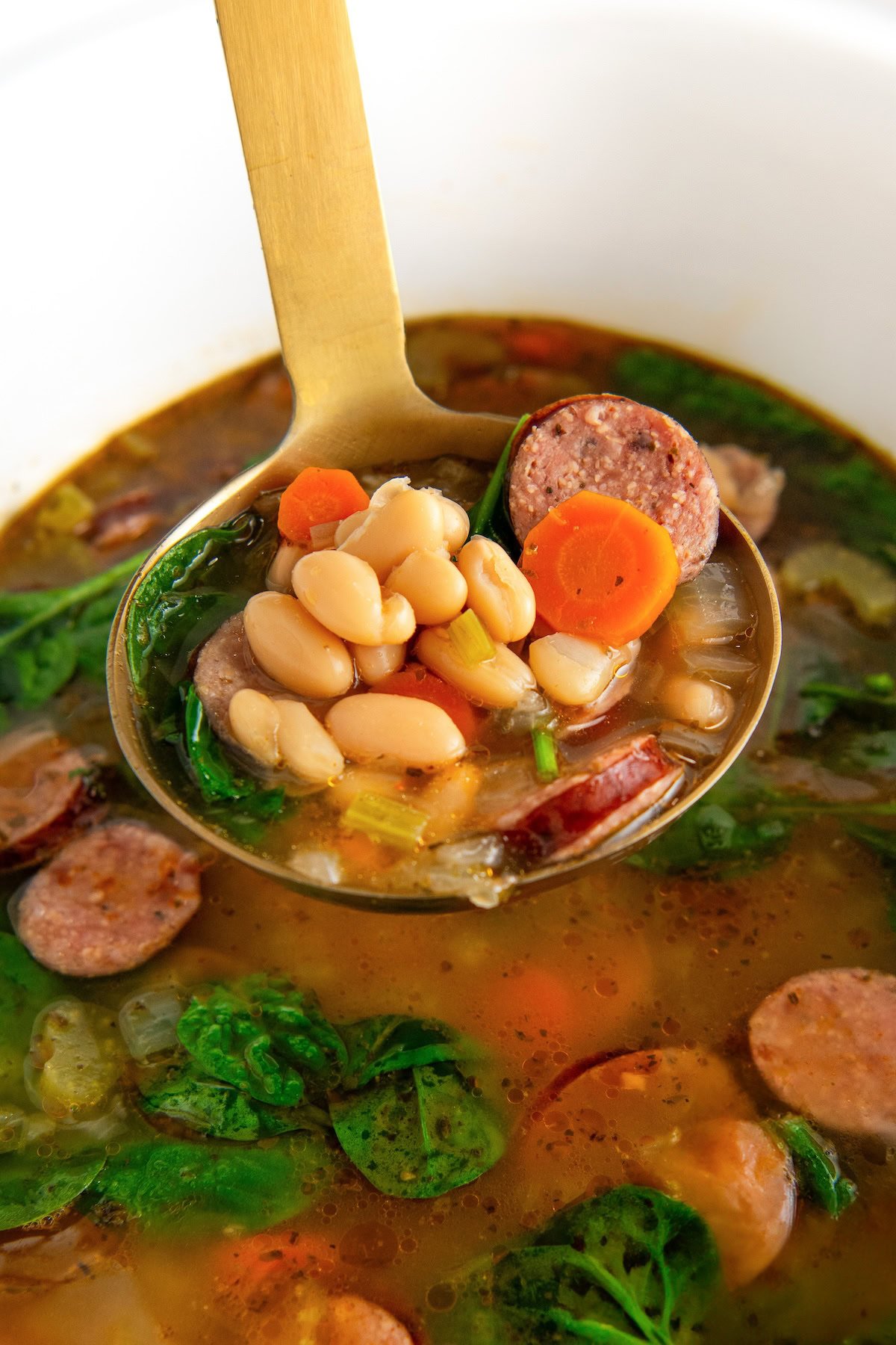 White bean and sausage soup being scooped out of a large slow cooker.