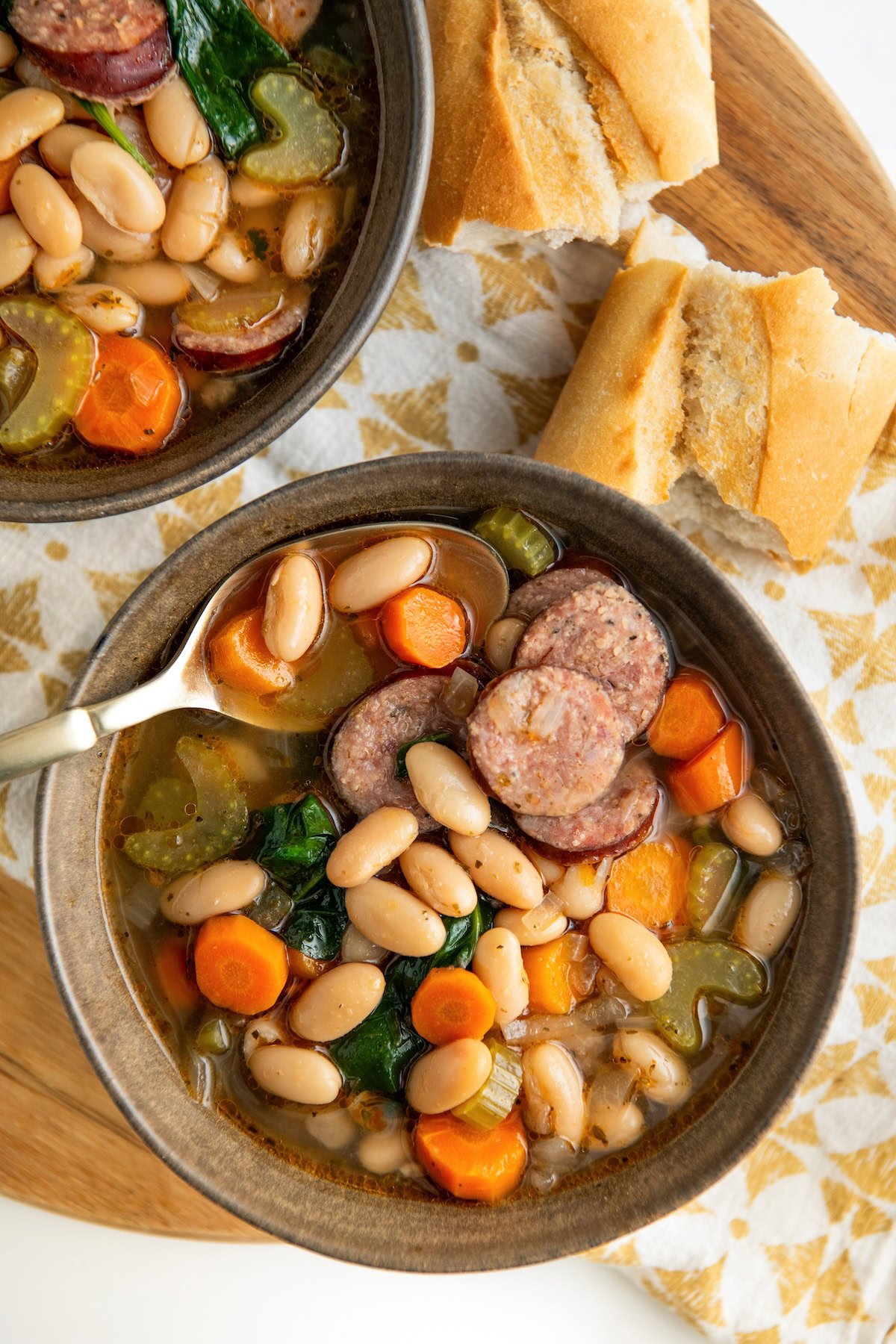 Crusty bread is placed next to two bowls of white bean and sausage soup.